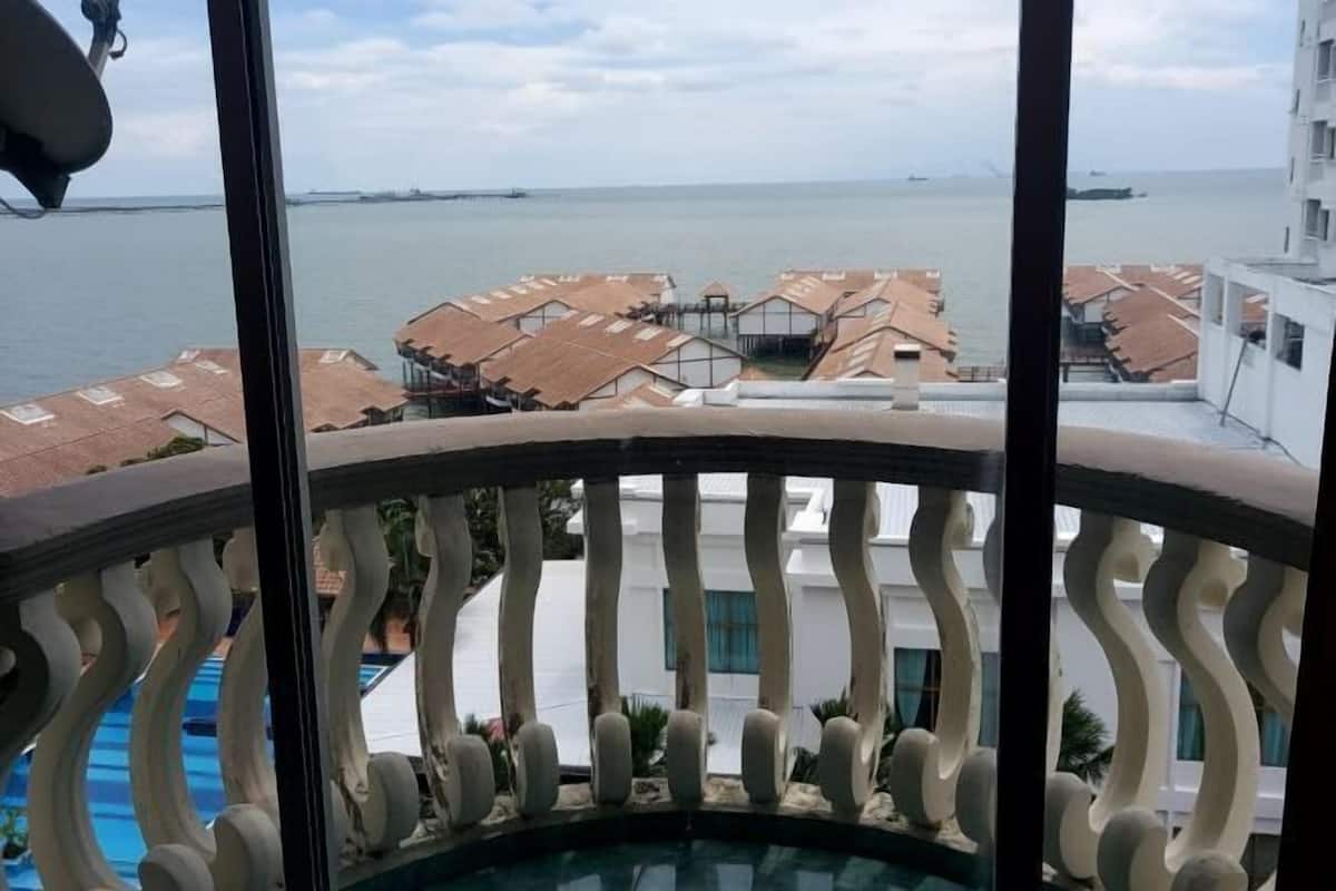 A balcony with a view of a coastal area, including buildings with red roofs and a body of water.