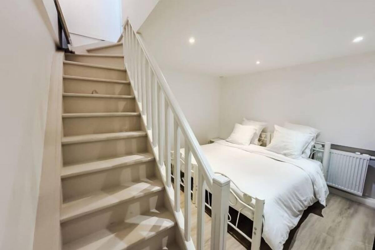 Une chambre à coucher avec un lit, des murs blancs, un escalier et un radiateur.