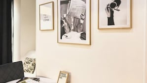 Una habitación con una cama, un cuadro con la imagen de una persona leyendo un periódico y una cita enmarcada en la pared.