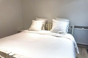 Ein Bett mit weißer Bettwäsche und Kissen, ein Nachttisch und eine Heizung.