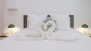 Una cama con ropa de cama blanca y dos lámparas verdes a cada lado.