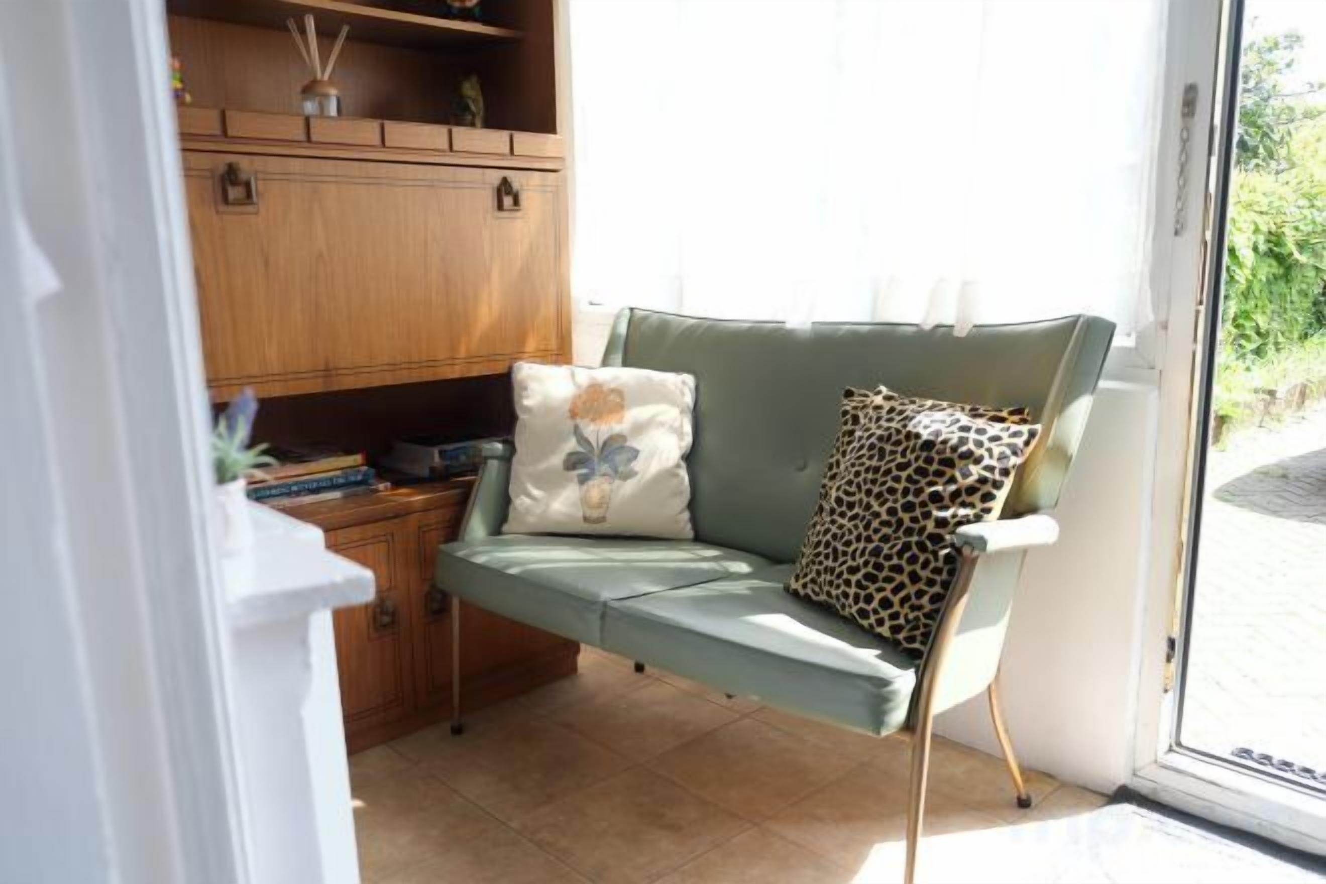 A room with a green sofa, a leopard print pillow, and a wooden cabinet.