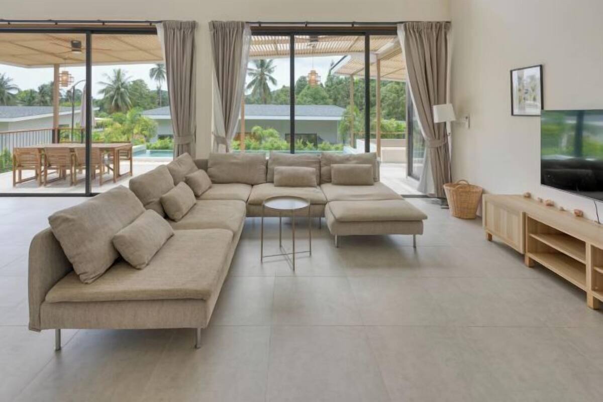 A modern living room with a beige sectional sofa, a small round table, and a TV on a wooden stand.