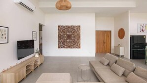 A modern living room with a large sectional sofa, a flat-screen TV, a decorative wall piece, and a small round table. - Tropical Peaceful Poolside Retreat by Sea N' Rent (Koh Phangan)