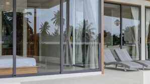 A modern room with a bed, a glass wall, and two lounge chairs. - Tropical Peaceful Poolside Retreat by Sea N' Rent (Koh Phangan)