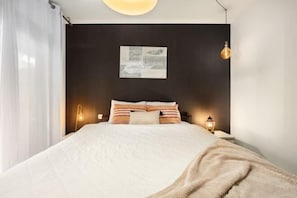 A modern bedroom with a dark headboard, a white bedspread, and two bedside lamps. - Royal Park Resort Apartment 55 (Eilat)