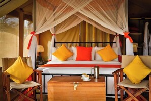 A bed with a canopy, two chairs, a bedside table, and a lamp.