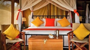 A bed with a canopy, two armchairs, a bedside table with a coffee pot, and a suitcase. - Kenzan Mara Camp (Serengeti)