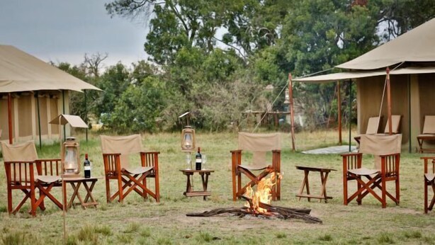 A campsite with tents, wooden chairs, tables, and a central fire. - Kenzan Mara Camp (Serengeti)