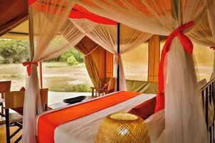 A tent-style room with a bed, a table, chairs, and a view of the outdoors.