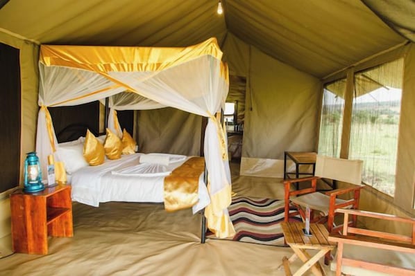 A tented accommodation with a canopy bed, a wooden nightstand, and a bench.
