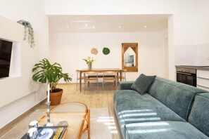 Ein Wohnzimmer mit einer Couch, einem Esstisch, einer Zimmerpflanze und einem Spiegel an der Wand.