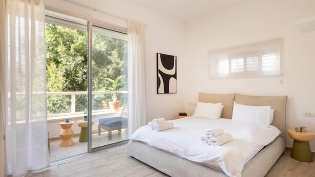 Une chambre à coucher avec un lit, une fenêtre avec des rideaux, une table de chevet et une œuvre d’art accrochée au mur.