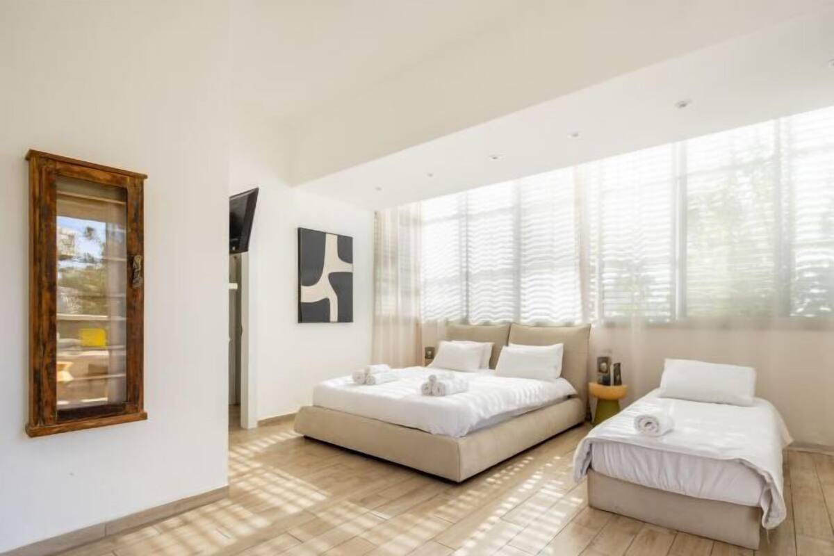Ein modernes Schlafzimmer mit einem großen Bett, einem kleineren Bett und einem Fenster mit Jalousien.