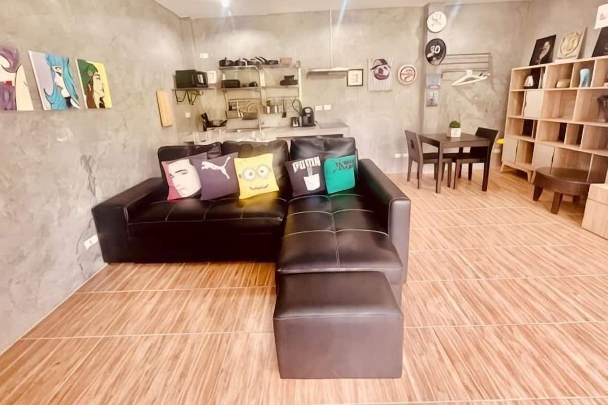 A modern living room with a black sectional sofa, a coffee table, and a dining area with a wooden table and chairs.