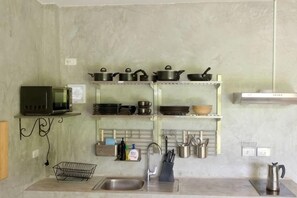 A kitchen with a microwave, shelves with pots and pans, a sink, and a kettle. - Destination 39 Pool Villa (Phuket)