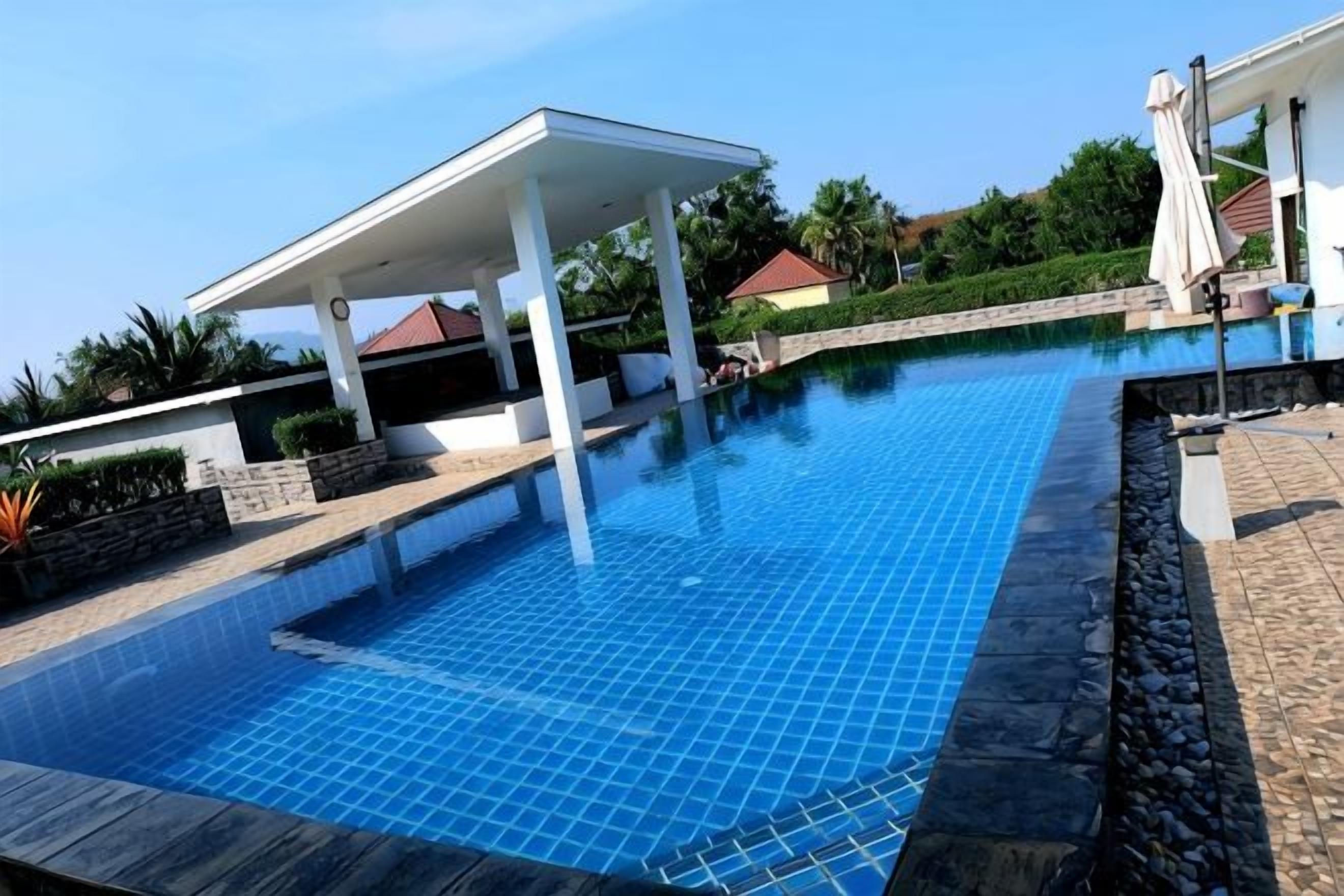 A swimming pool with a covered area, stone edging, and a clear blue sky.