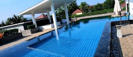 A swimming pool with a covered area, stone edging, and a clear blue sky.