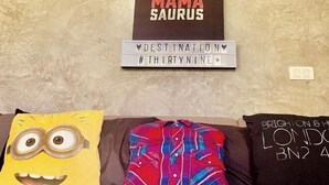 A room with a brown couch, a Minion pillow, a Destination sign, and a London pillow. - Destination 39 Pool Villa (Phuket)