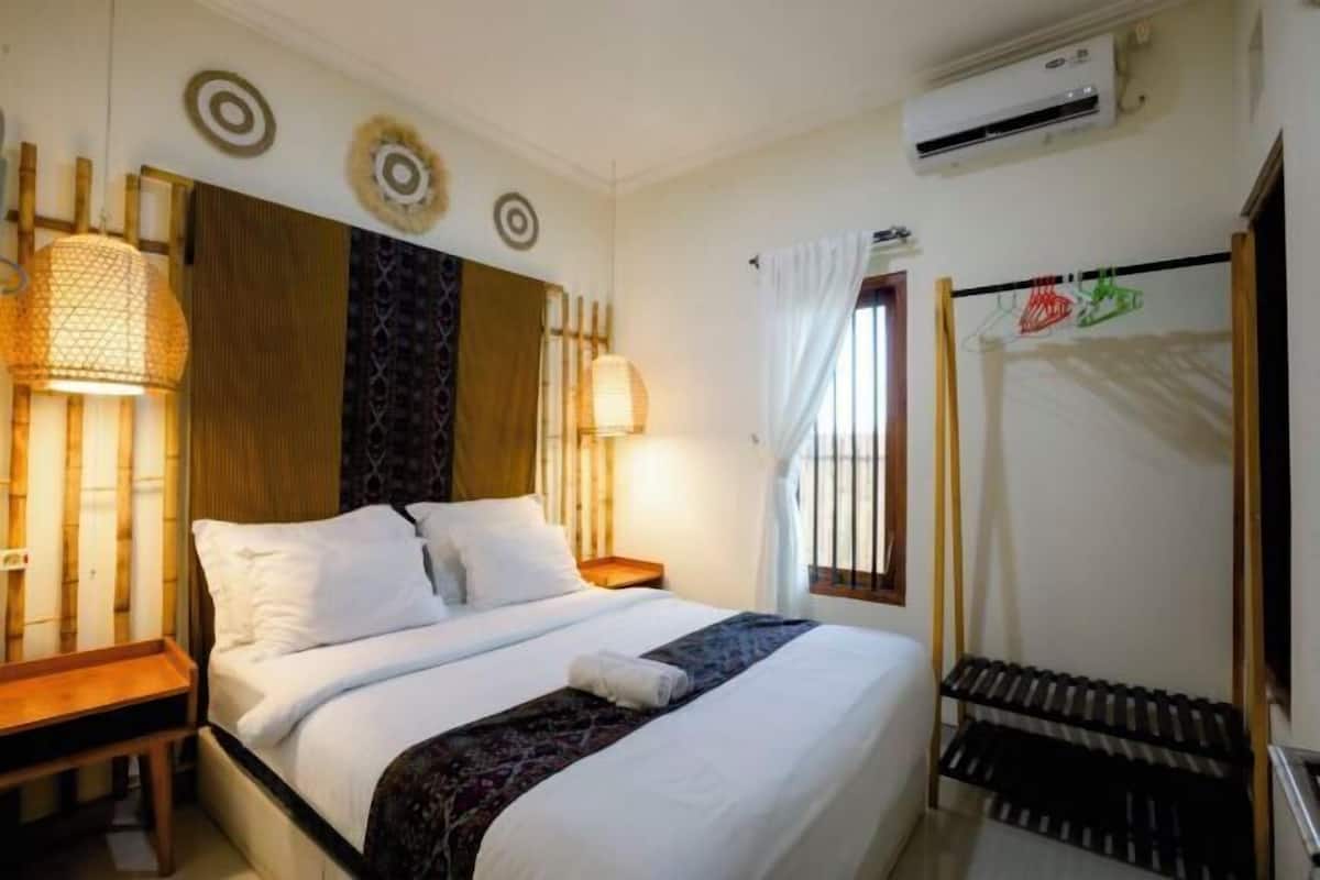 A hotel room with a bed, bedside lamps, an air conditioning unit, and a window with curtains.