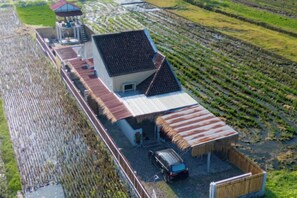 A large building with a covered outdoor area, adjacent to a field. - Villa New D'Bamboo by Plesirhatiyogja (Sewon)