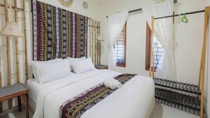 A bed with a patterned bedspread, a bedside table, and a wall-mounted air conditioning unit. - Villa New D'Bamboo by Plesirhatiyogja (Sewon)