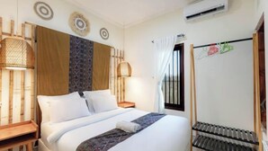 A hotel room with a bed, bedside tables, a window with curtains, and a wall-mounted air conditioner. - Villa New D'Bamboo by Plesirhatiyogja (Sewon)