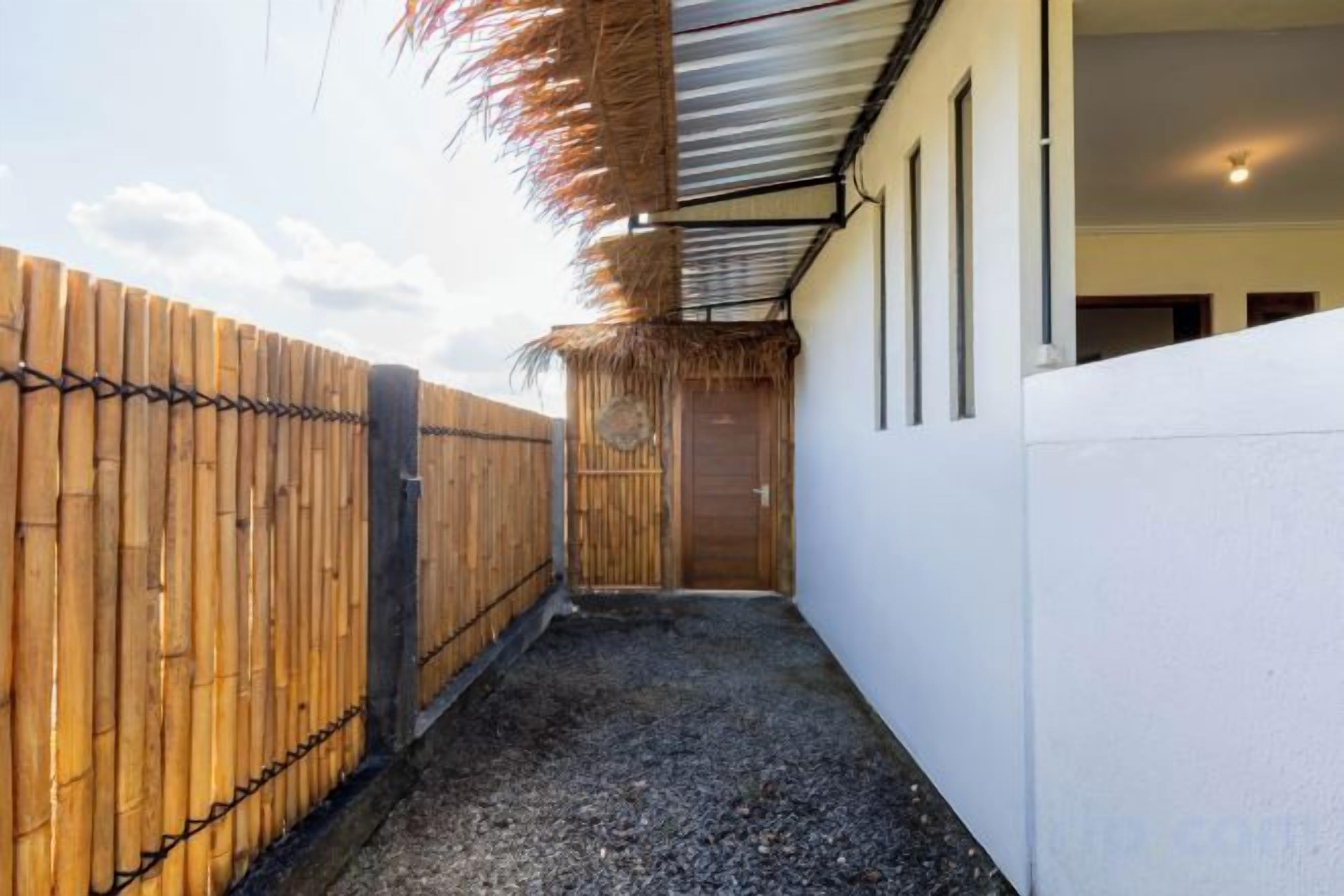 Un pasillo estrecho con una valla de madera a un lado y una pared blanca al otro, que conduce a una puerta.
