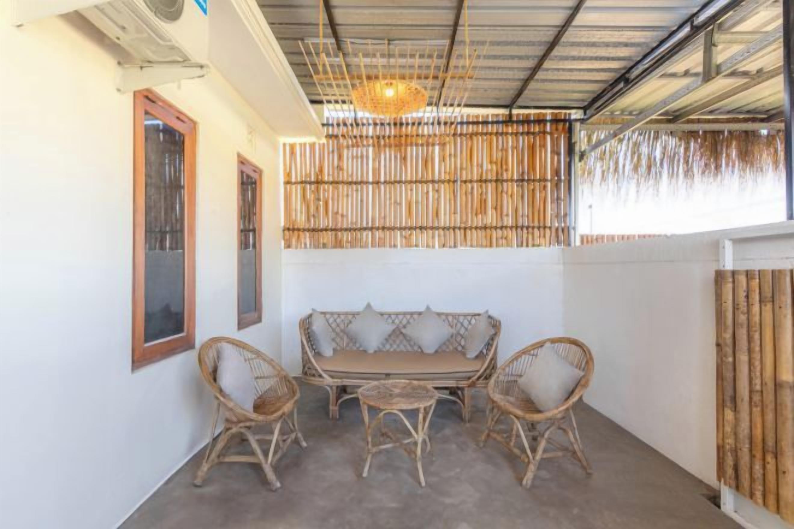 A covered outdoor seating area with a bamboo wall, a cushioned bench, and wicker chairs.