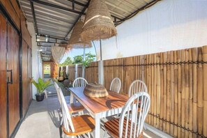 Un área de comedor al aire libre con mesa y sillas de madera, un toldo tejido y una valla de bambú.