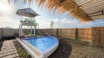A swimming pool with a pergola and a gazebo, surrounded by a wooden fence and a stone pathway.