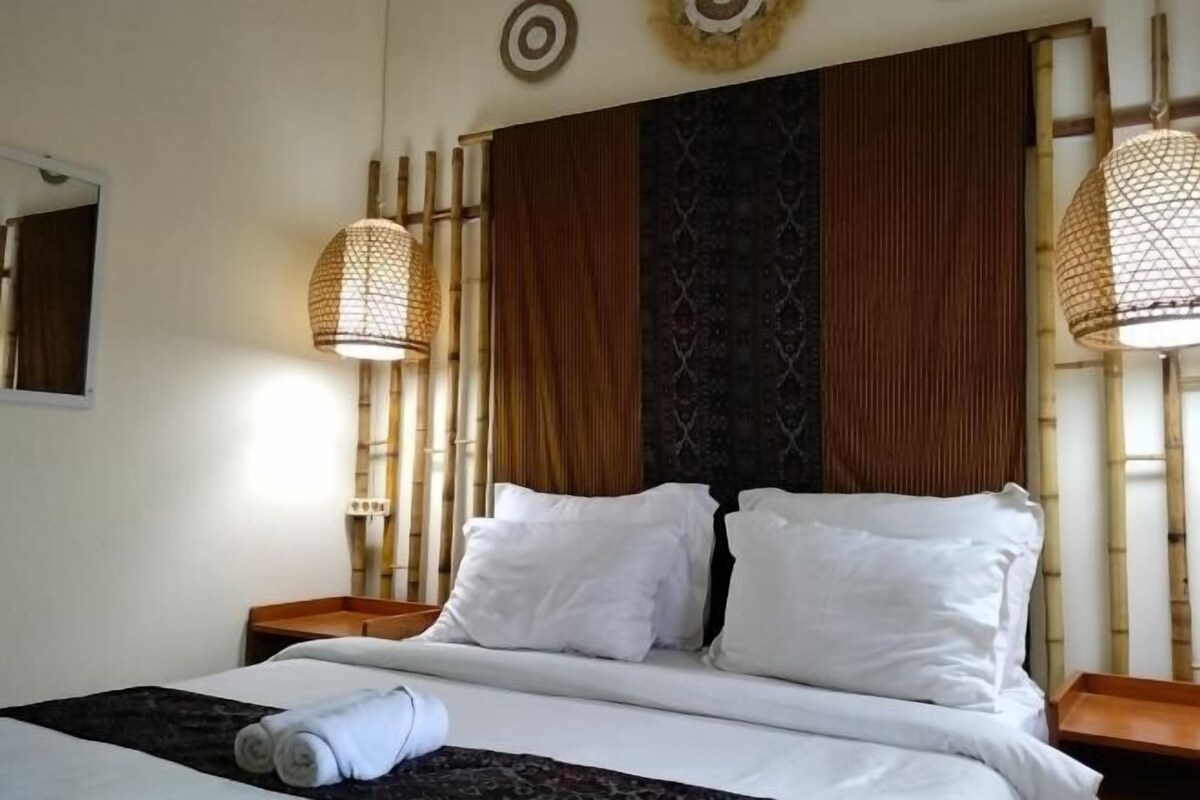 A hotel room with a bed, two bedside tables, a mirror, and two wall-mounted lamps.