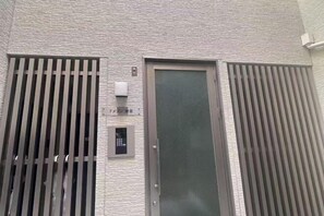 A building with a textured facade, a metal door with a security keypad, and two vertical metal bars on either side. - New open！F Maison Kishinosato｜Next to Tenga Chaya Park (Osaka)