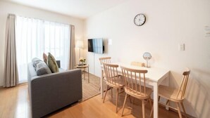 A modern living room with a sofa, dining table, chairs, a TV, and a clock on the wall. - New open！F Maison Kishinosato｜Next to Tenga Chaya Park (Osaka)