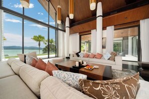 A modern living room with a large sofa, a coffee table, and a view of the ocean. - Luxury Beachfront Villas & Resort (Phuket)