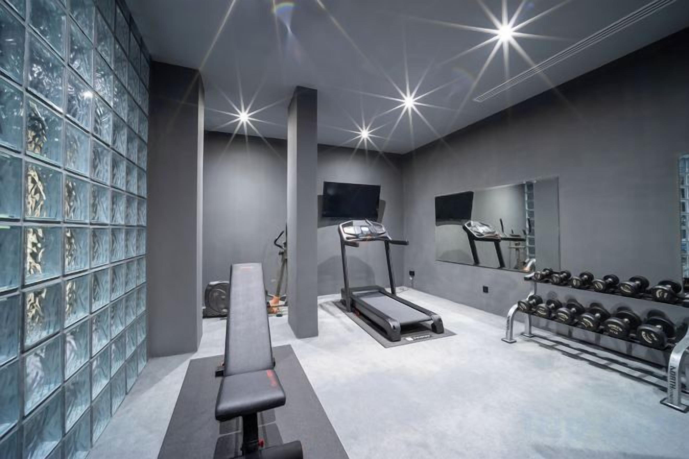 A gym with a bench, treadmills, and a rack of dumbbells.