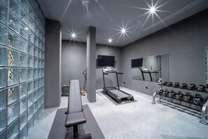 Une salle de sport équipée d’un banc, de tapis de course et d’un porte-haltères.