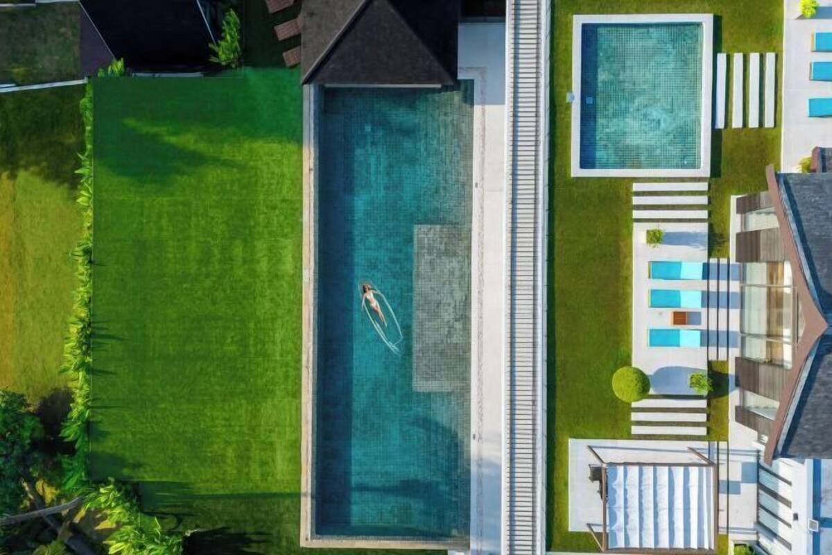 An aerial view of a property with a large rectangular swimming pool, a smaller pool, and a covered outdoor seating area.