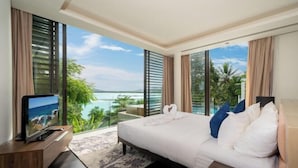 A modern hotel room with a large bed, a flat-screen TV, and a balcony with a view of the sea. - Luxury Beachfront Villas & Resort (Phuket)