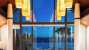 A modern hotel lobby with large windows, a pool, and a view of the mountains. - Luxury Beachfront Villas & Resort (Phuket)