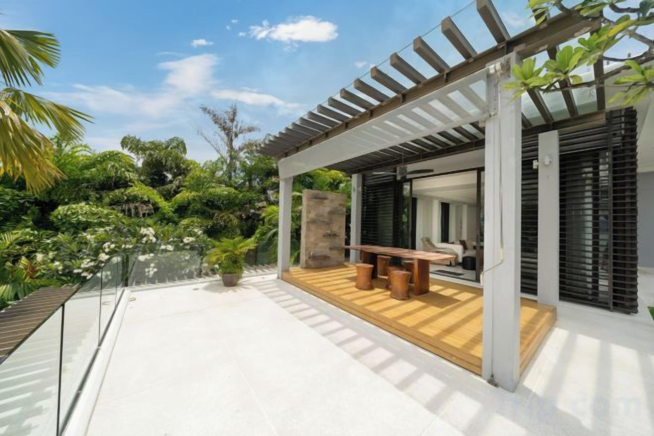 A modern outdoor patio with a wooden deck, a seating area, and a pergola structure.