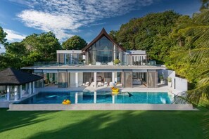 Une maison moderne dotée d’une grande façade vitrée, d’une piscine et d’une végétation luxuriante.