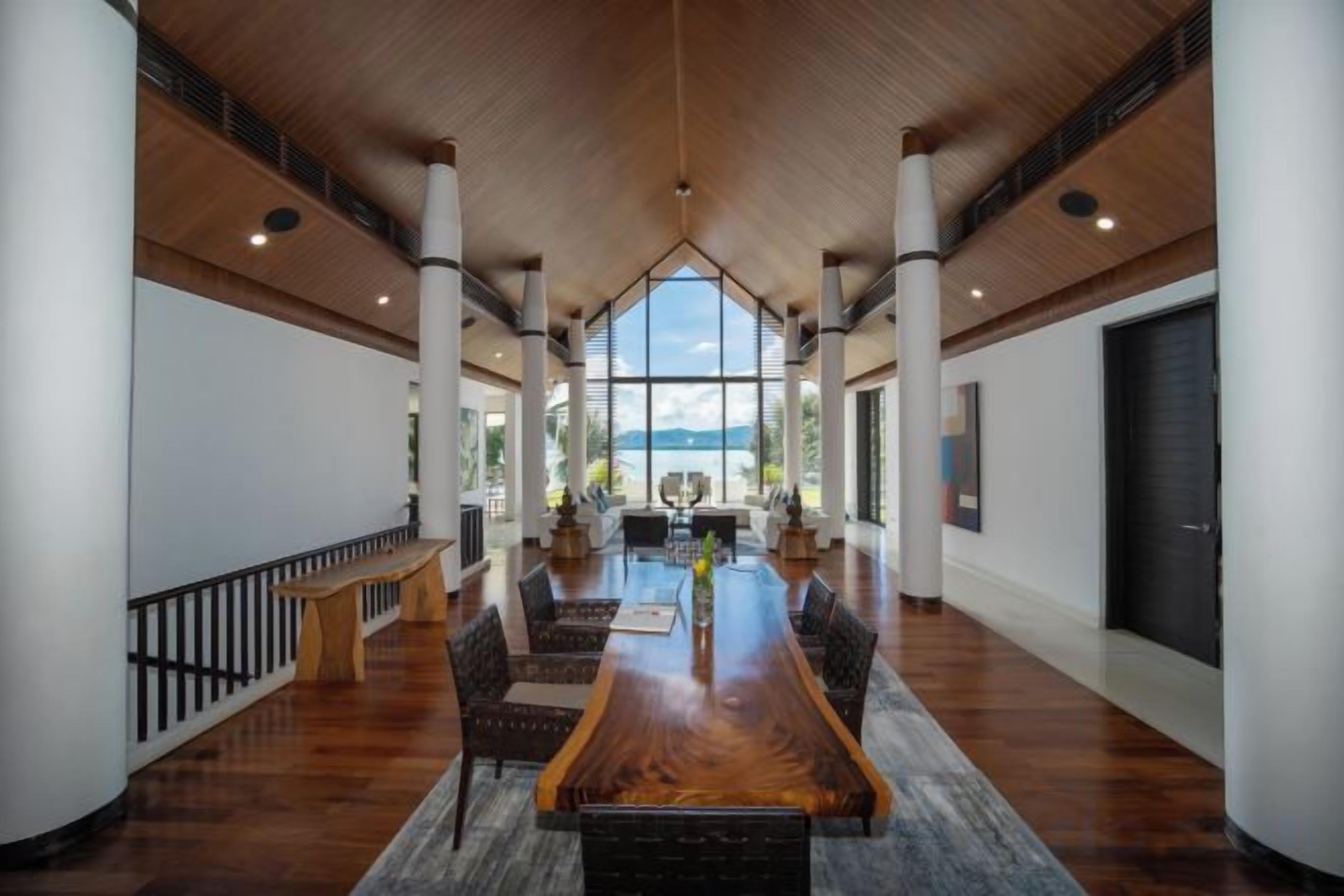 A spacious indoor area with a long wooden table, seating, and a view through large windows.