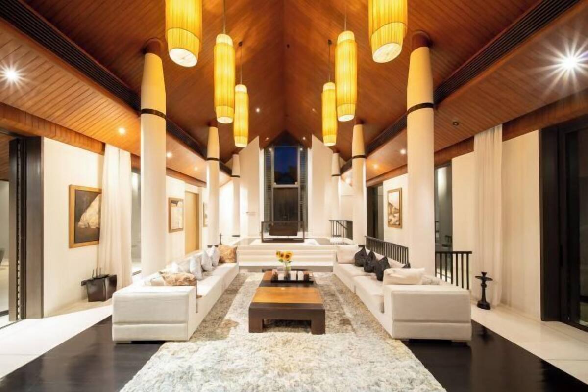 A spacious living room with a high ceiling, large windows, and a central seating area with sofas and a coffee table.