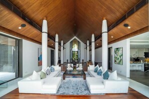 Un vaste espace de vie doté d’un haut plafond en bois, d’une table basse centrale et de canapés blancs agrémentés de coussins.