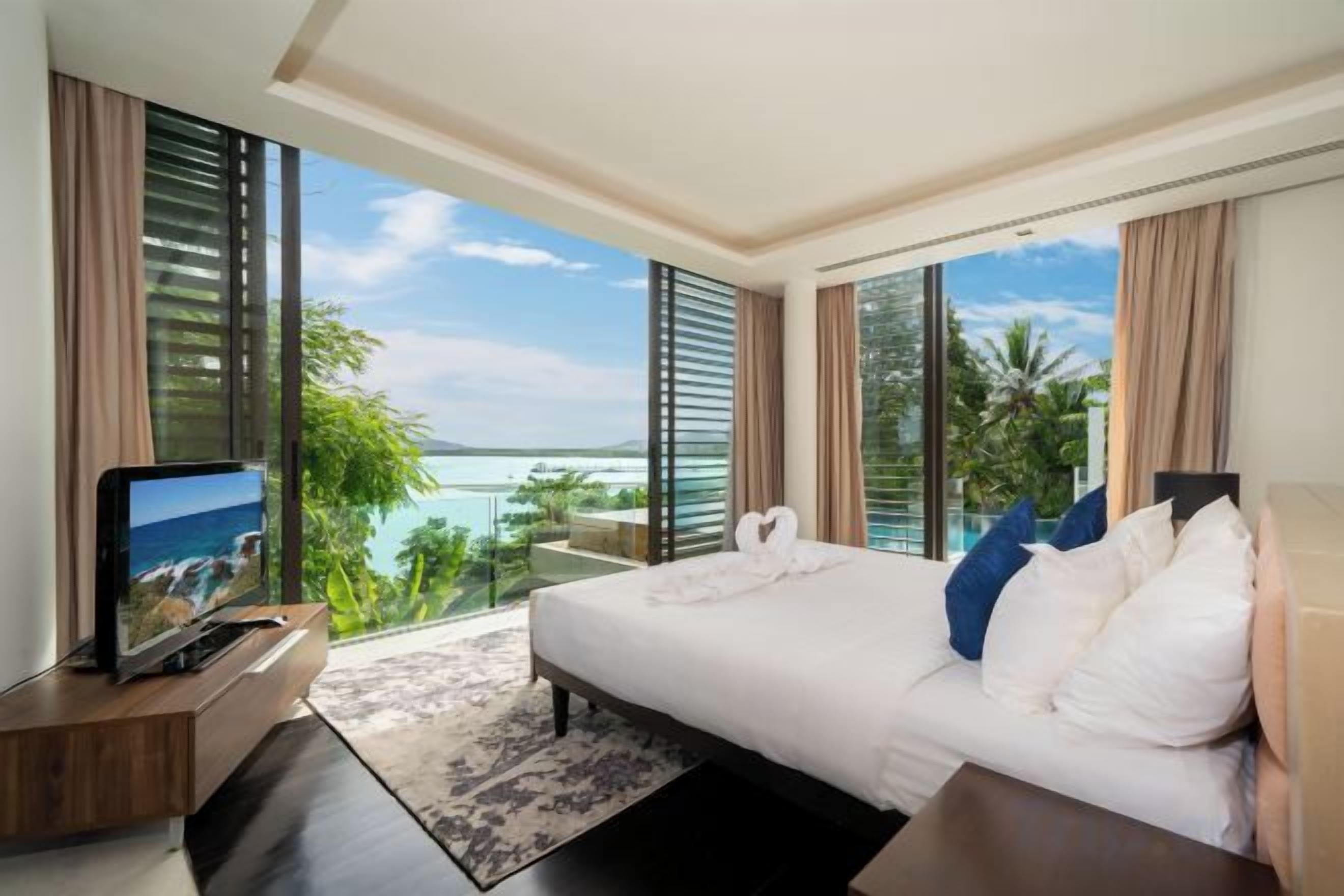 A hotel room with a large bed, a TV, and a balcony with a view of the sea.
