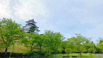 Um pagode japonês tradicional, com telhado em vários níveis, cercado por árvores verdes e uma área murada.