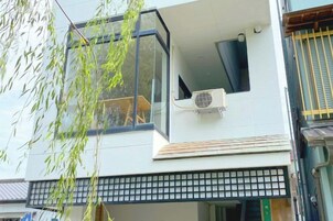 Edificio moderno con balcón, unidad de aire acondicionado y vista a un árbol.