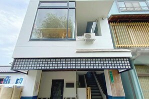 A two-story building with a flat roof, a visible air conditioning unit, and a covered entrance area. - JOKA BASE (Kakegawa)