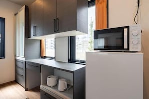 A modern kitchen with grey cabinets, a white refrigerator, and a microwave. - KAIGAN HAJIME HUB (Tokyo)